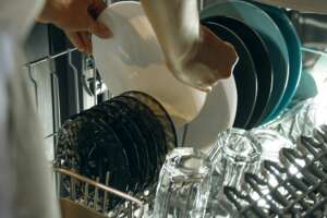 Female hands taking out clean plate from open dishwasher.